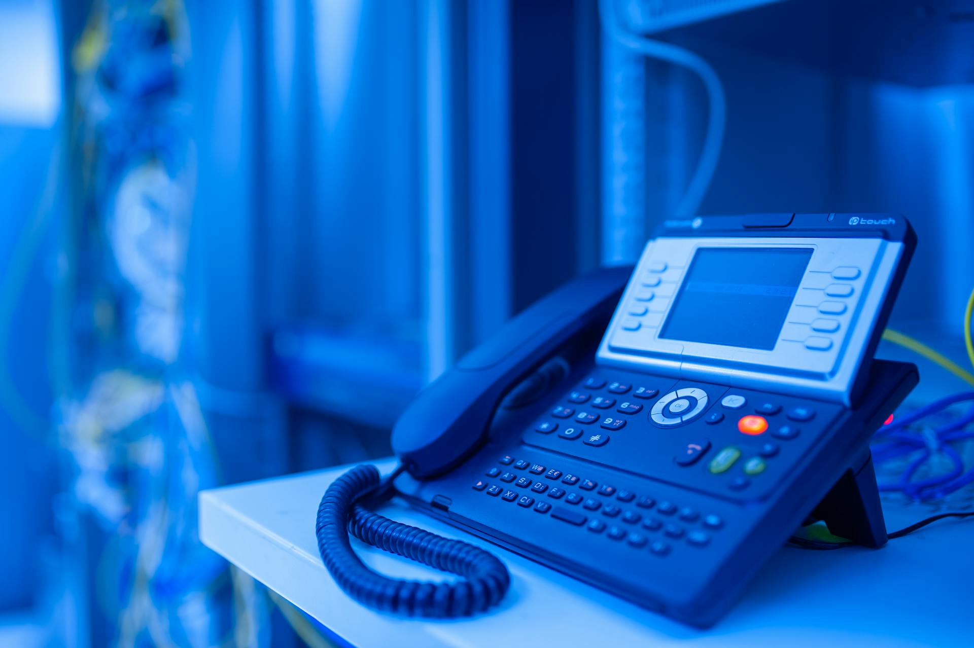 A VoIP phone sits on an office desk in a dark room. 